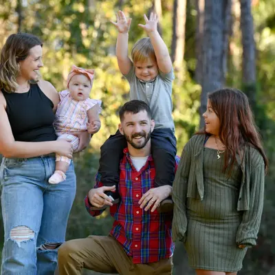 Family of five smiling in a forest, with a man holding a young boy on his shoulders.