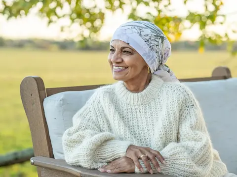 Smiling Elderly Woman In Cream Knit Sweater Sitting On Outdoor Bench With Head Scarf
