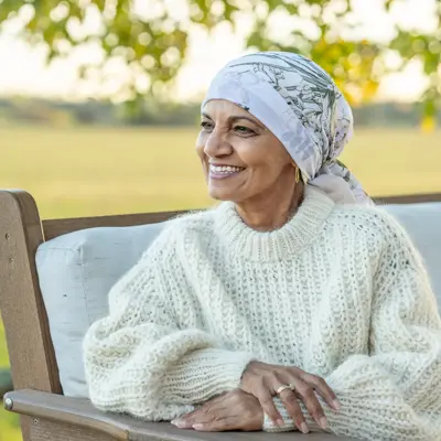 Smiling Elderly Woman In Cream Knit Sweater Sitting On Outdoor Bench With Head Scarf