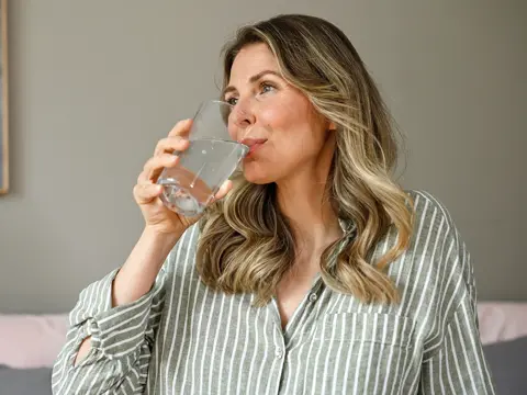 Woman in green and white striped pajamas drinking a glass of water in a bright, modern living room