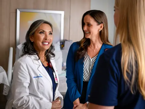 Three smiling AdventHealth employees in a hospital room, discussing patient care.