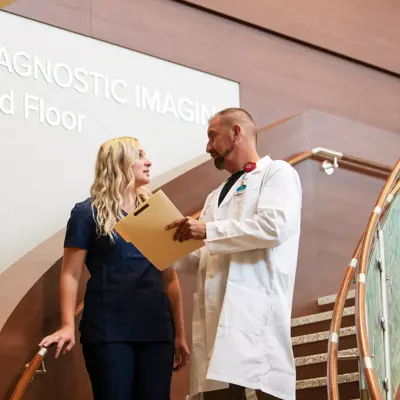 Doctor and nurse discussing patient records near a staircase in a hospital.