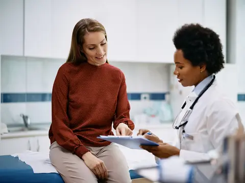 African American doctor and her female patient analyzing medical report after examination in the hospital. Focus is on female patient.