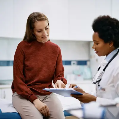 African American doctor and her female patient analyzing medical report after examination in the hospital. Focus is on female patient.