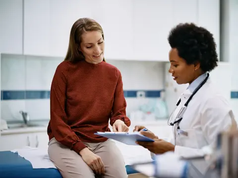 African American doctor and her female patient analyzing medical report after examination in the hospital. Focus is on female patient.