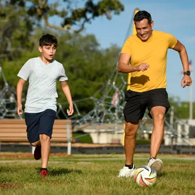 A father and son playing soccer in a park, showcasing active family bonding and outdoor fun.