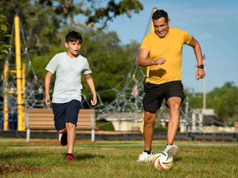 A father and son playing soccer in a park, showcasing active family bonding and outdoor fun.