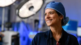 Smiling female surgeon in blue scrub cap looking upward in an operating room with surgical lights visible in the background