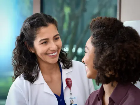 A smiling doctor in a white coat talks to a patient, conveying warmth and care.