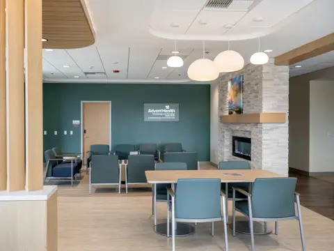 Modern medical facility waiting room with teal accent wall, comfortable seating arrangements, pendant lighting, stone fireplace, and AdventHealth Hematology and Oncology branding