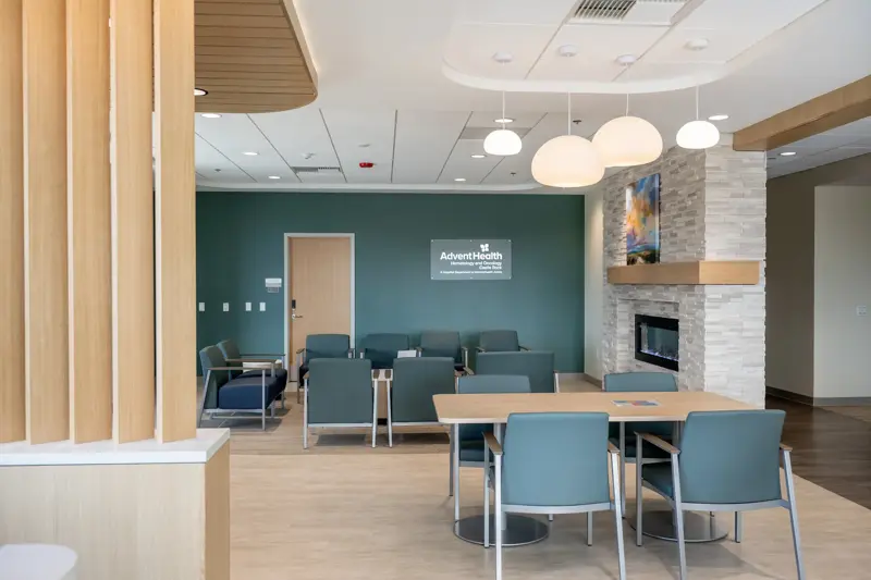 Modern medical facility waiting room with teal accent wall, comfortable seating arrangements, pendant lighting, stone fireplace, and AdventHealth Hematology and Oncology branding