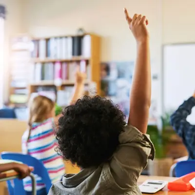 Students raising their hands to answer a question during a classroom lesson.