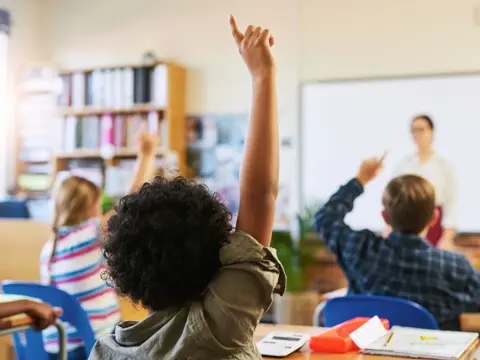 Students raising their hands to answer a question during a classroom lesson.