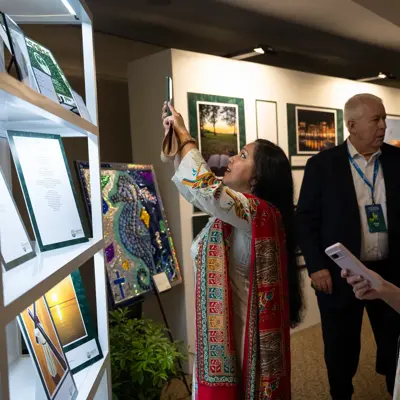 Three attendees view a lit display of framed artwork and documents, with one person holding up a phone.