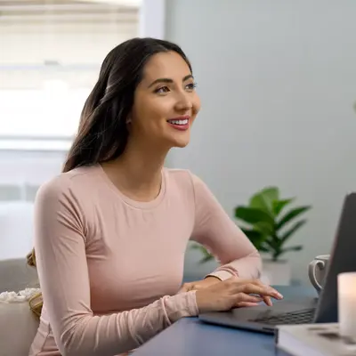 Smiling woman working on laptop at home with candle and plants.