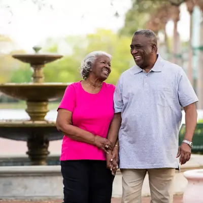 Elderly couple smiling and holding hands in front of a fountain.
