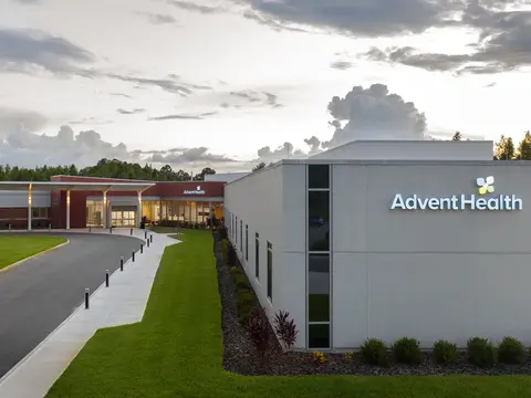 Exterior view of AdventHealth Connerton facility at dusk with illuminated entrance, manicured landscaping, and dramatic cloudy sky