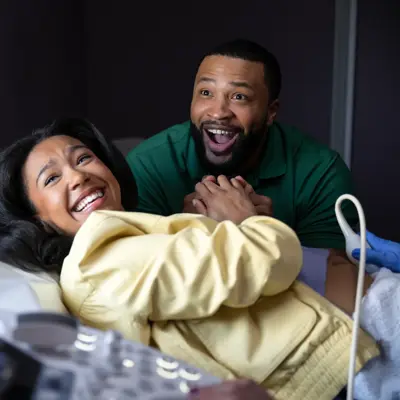 A smiling pregnant woman and her partner in a hospital room, looking at an ultrasound screen.