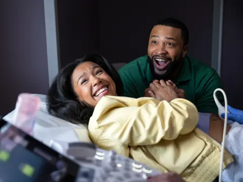 A smiling pregnant woman and her partner in a hospital room, looking at an ultrasound screen.