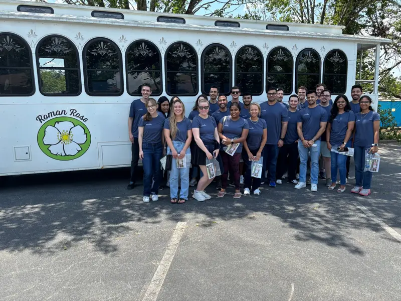 Group in matching shirts posing in front of a white trolley labeled “Roman Rose.”