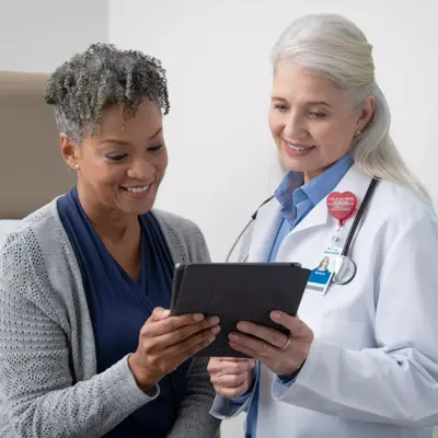 A smiling doctor and patient look at a tablet together in a medical office.