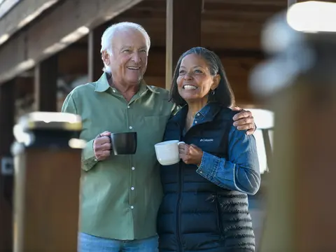 Smiling couple standing together holding coffee mugs outdoors in front of a modern home
