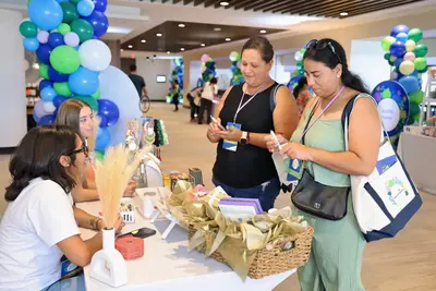 Two attendees standing at a vendor table examining wellness products while two team members seated behind the table assist them at the AdventHealth Women's Health and Cancer Prevention Event