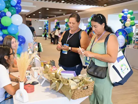 Two attendees standing at a vendor table examining wellness products while two team members seated behind the table assist them at the AdventHealth Women's Health and Cancer Prevention Event