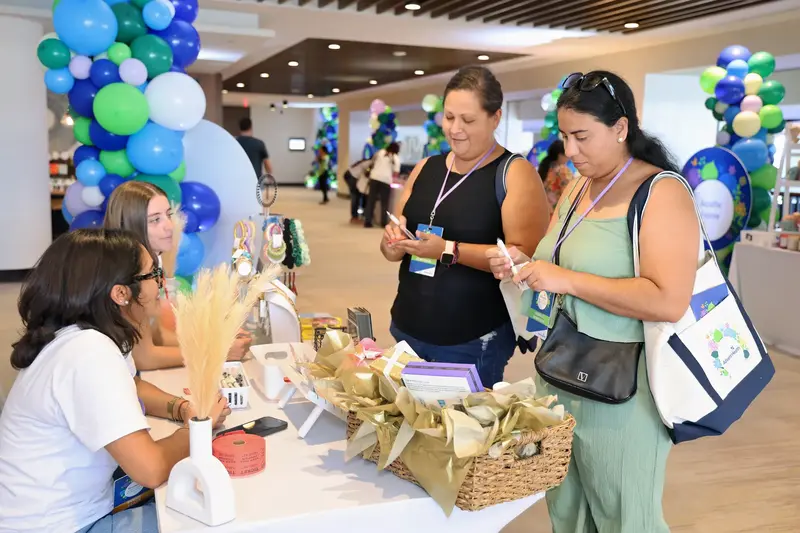 Two attendees standing at a vendor table examining wellness products while two team members seated behind the table assist them at the AdventHealth Women's Health and Cancer Prevention Event
