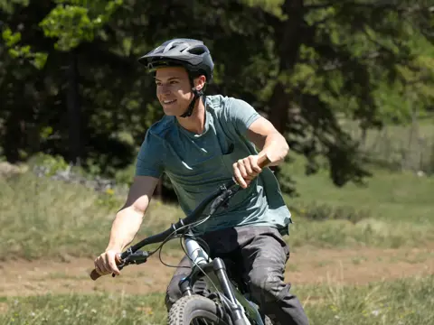 A man wearing a helmet rides a mountain bike on a dirt trail in a forest.