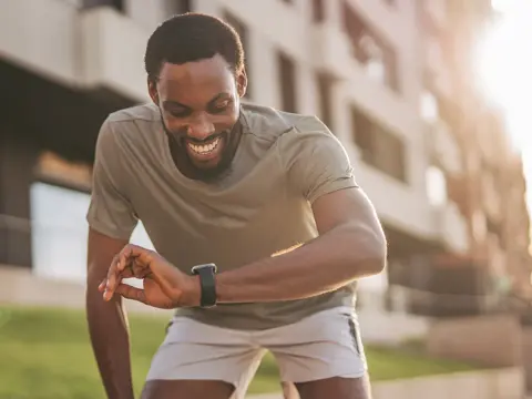 A male runner smiling and looking at his watch.