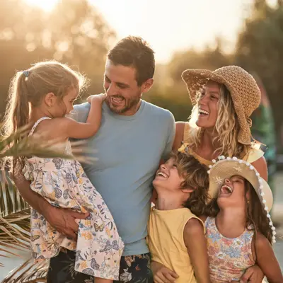 Smiling family of five outdoors at sunset, with parents holding and hugging three laughing children.