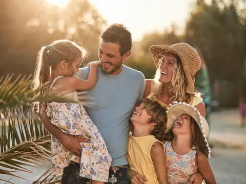 Smiling family of five outdoors at sunset, with parents holding and hugging three laughing children.