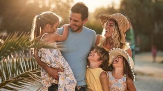 Smiling family of five outdoors at sunset, with parents holding and hugging three laughing children.