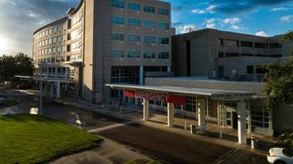 Modern hospital building with emergency entrance and red sign, under a partly cloudy blue sky.