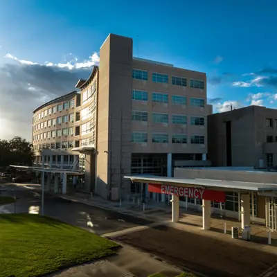 Modern hospital building with emergency entrance and red sign, under a partly cloudy blue sky.