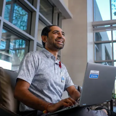 A smiling man in a hospital lounge using a laptop, conveying a sense of comfort and productivity.