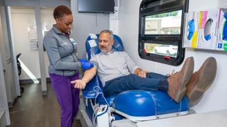 A nurse is preparing to draw blood from a patient seated in a blue chair.