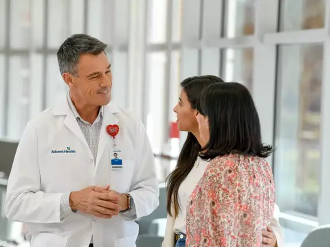 A doctor in a white coat talks with two women in a hospital waiting room.