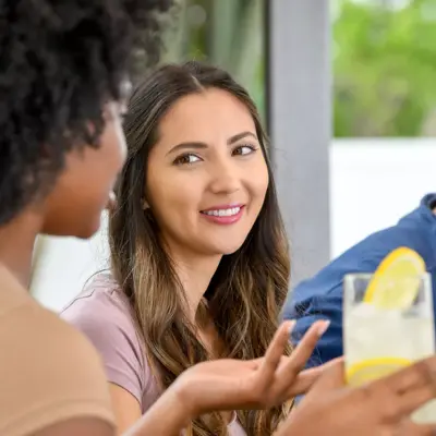 A smiling woman engages in conversation with another woman, holding a glass of lemonade.