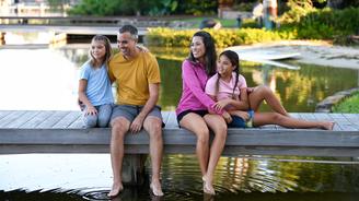 Family of four smiling and sitting on a dock by a lake.