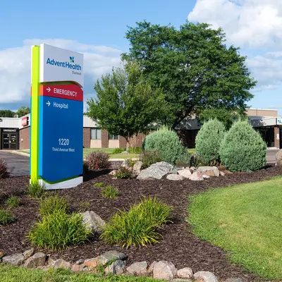 AdventHealth Durand sign with emergency and hospital directions, set in a landscaped area with greenery and a clear blue sky.