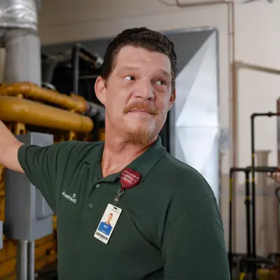 A man in a green polo shirt stands next to a large yellow machine, smiling at the camera.