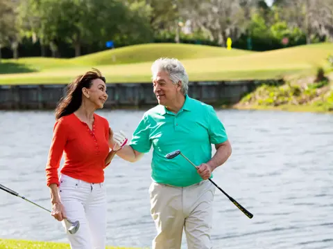 Elderly couple walking on a golf course, holding hands and smiling.