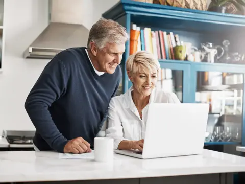 A Senior Couple Looks at a Laptop Together in Their Kitchen
