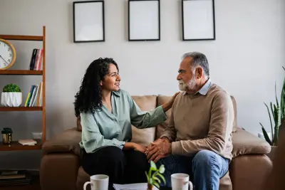 An older man sits on a couch, being comforted by a female therapist.
