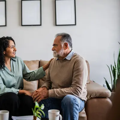 An older man sits on a couch, being comforted by a female therapist.