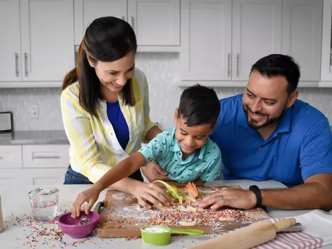 Family of three smiling and baking together in a modern kitchen.