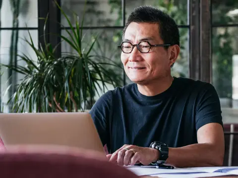 Smiling man in glasses and watch working on laptop in a bright office with plants.