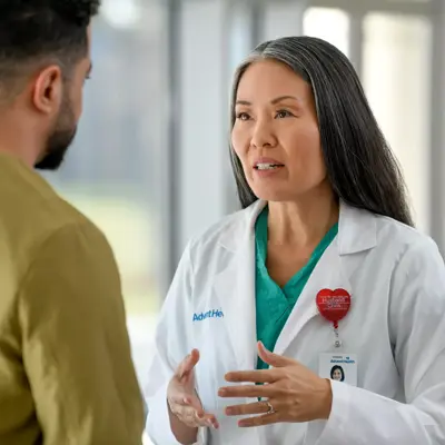 A female doctor in a white coat is talking to a male patient in a hospital corridor.